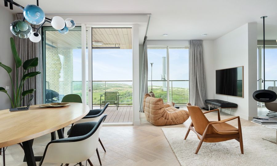 lichtgrijze eiken visgraat in kleurrijk interieur met Seal lounge chair van Ib Kofod-Larsen, Bocci 28 armature boven de eettafel en Togo van Ligne Roset voor de extra grote TV in Schevenings penthouse | The Woodstore Scheveningen